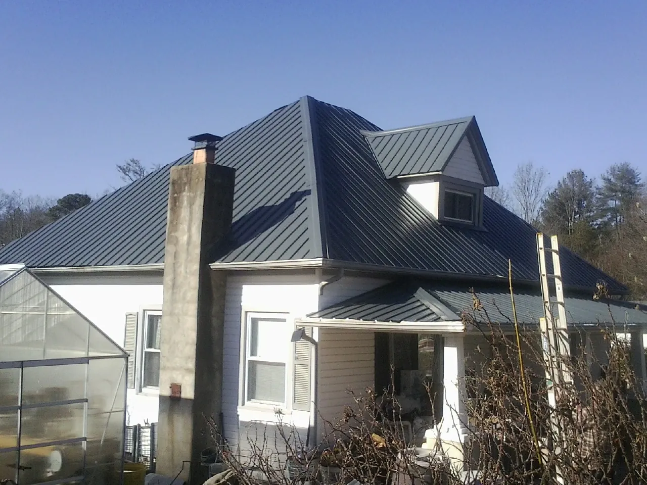 Dark blue standing seam metal roof on a white farmhouse with dormer — Slate & Tile Roof Repair by Roofing Brothers in Stokesdale