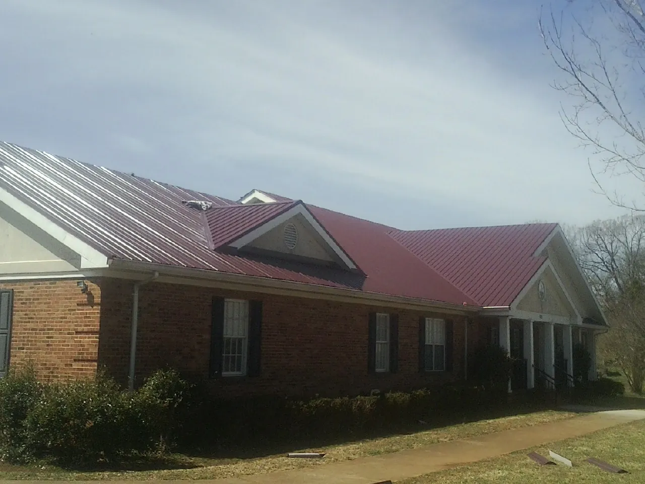 Red metal roof with gabled entries on a long brick building, from a Hail Damage Roof Repair job in Stokesdale