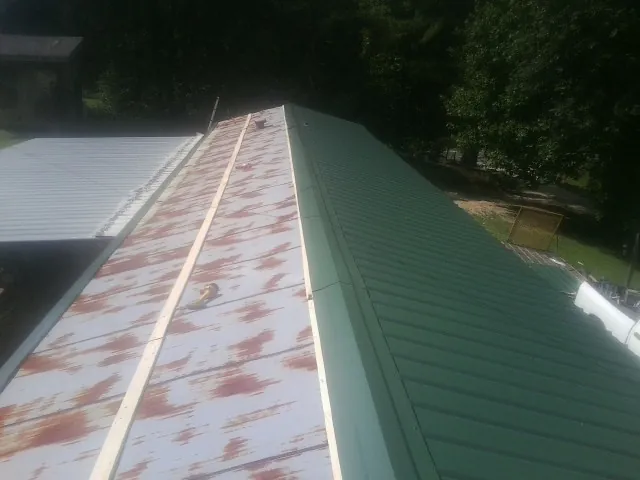 Old rusted panels beside newly installed green metal roofing — Wind Damage Roof Repair by Roofing Brothers in Stokesdale