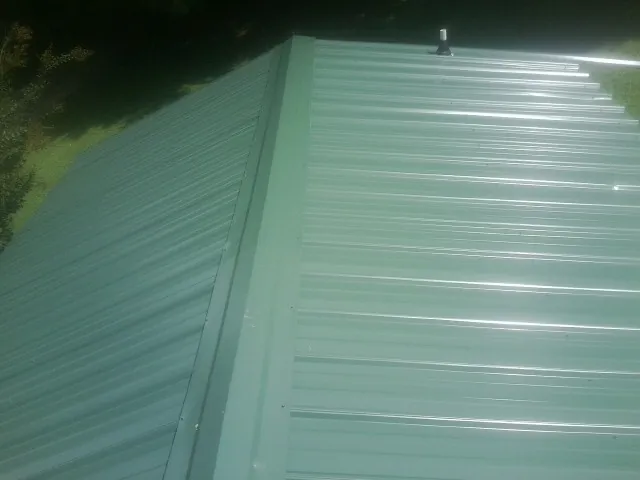 New green metal panels meeting at the ridge of a roof — Flat Roof Repair work by our crew in Stokesdale