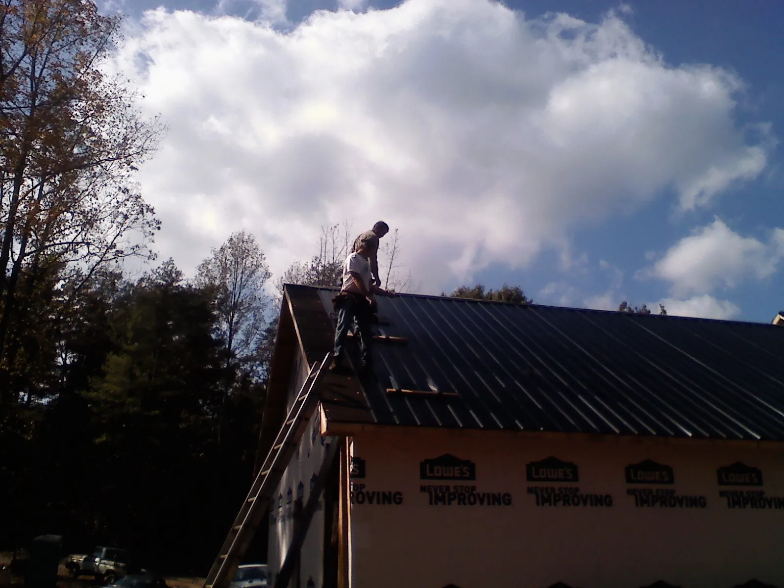 Roofer fastening dark metal panels high against a cloudy sky, from a Roof Inspection job in Stokesdale