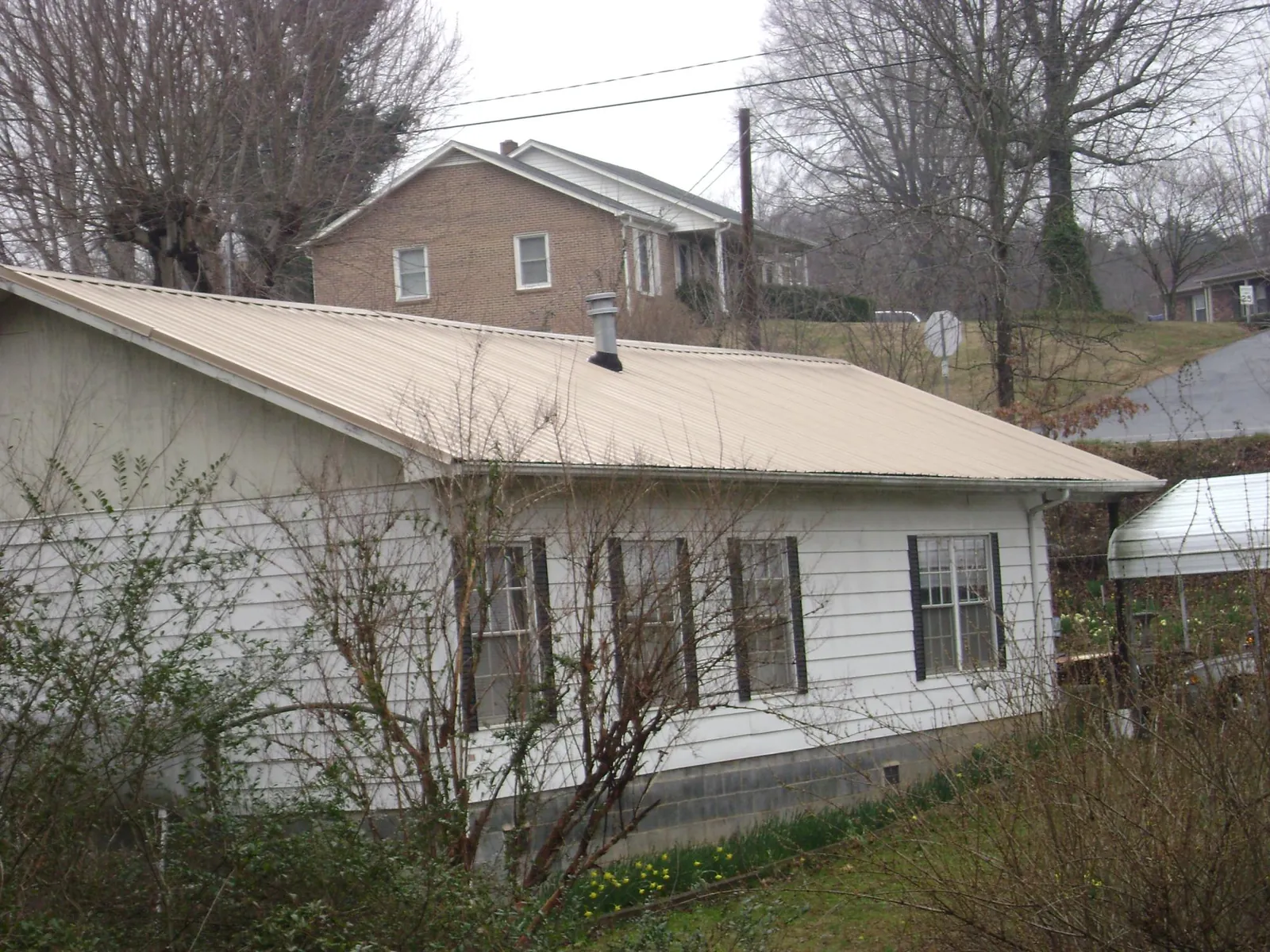 Tan metal roof on a white sided house set into a hillside — Commercial Roofing by Roofing Brothers in Stokesdale