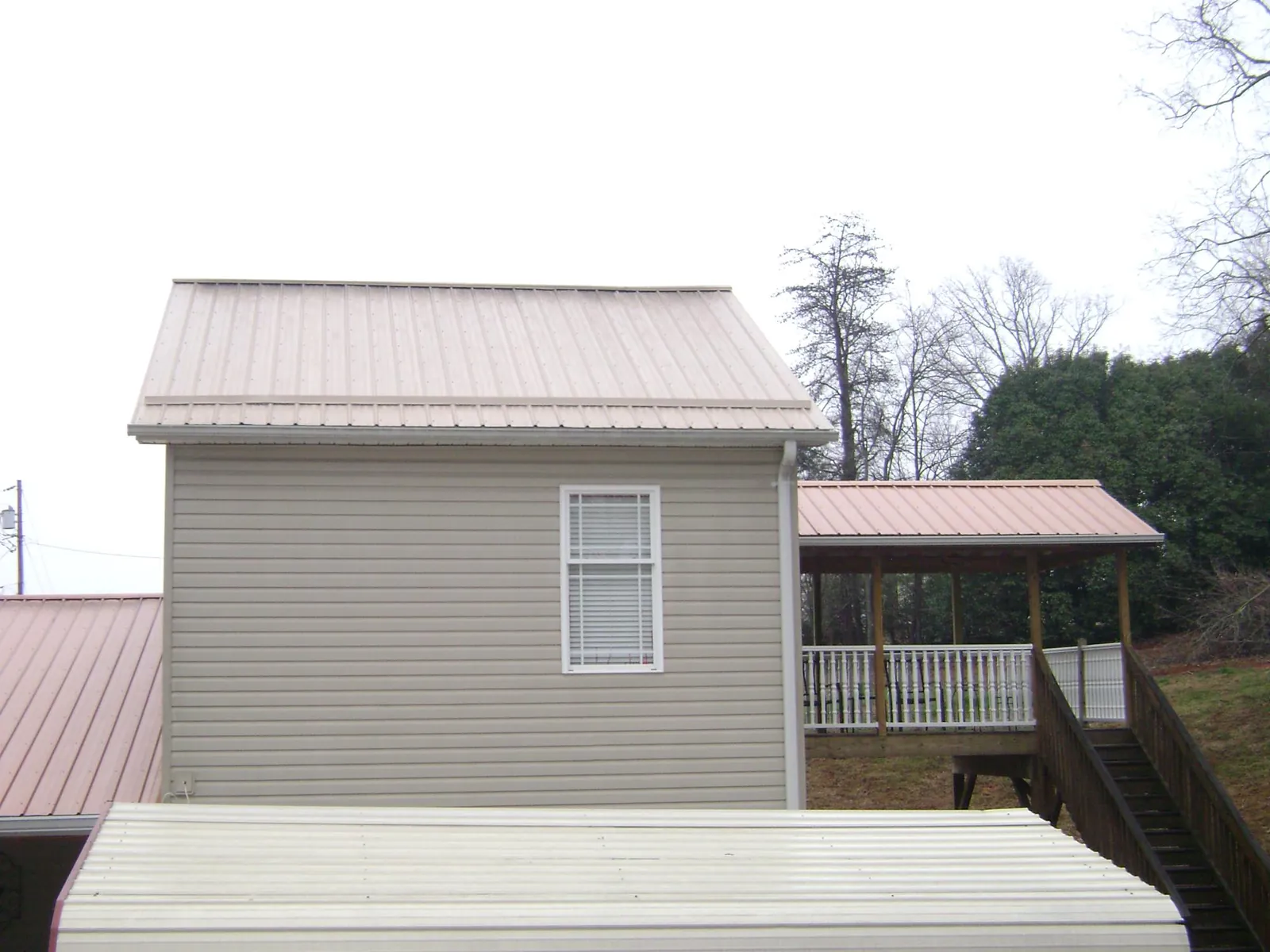 Tan metal roofs on a two story addition and attached porch, from a Roof Replacement job in Stokesdale