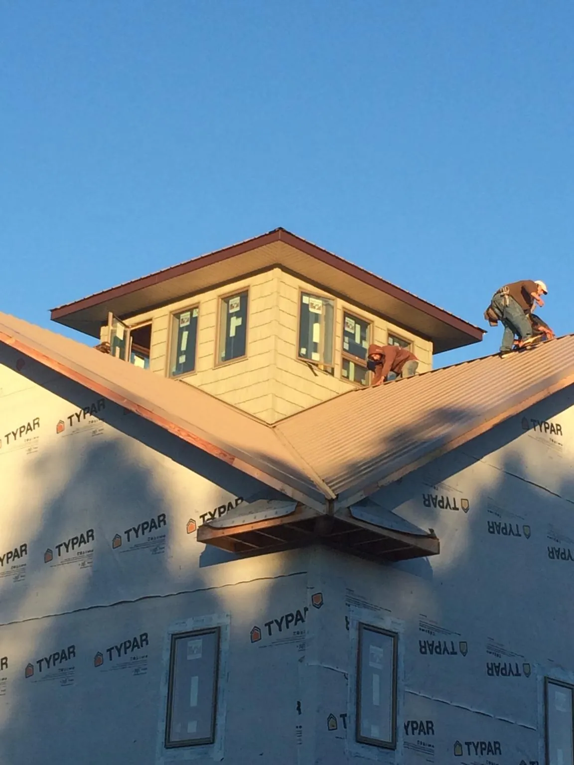 Roofers working around a rooftop cupola on a new metal roof at sunset — Roof Waterproofing in Stokesdale by Roofing Brothers